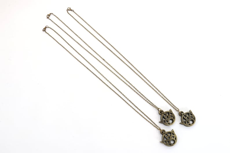 May include: Three gold necklaces with intricate pendant charms. Each charm features a detailed design with a circular shape and a pointed top.