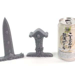 May include: Three gray 3D printed miniature swords, one with a long blade and two with shorter blades. The swords are on a white surface. A can of Japanese beer is in the background.