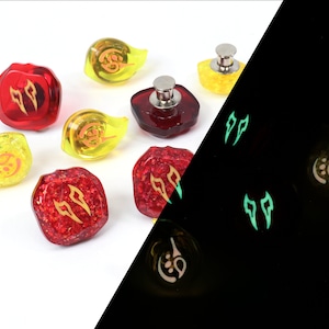 May include: Set of red and yellow dice with glow-in-the-dark features. The dice have a variety of symbols, including flames and a crescent moon. The dice are shown in both normal light and in the dark, highlighting their glow-in-the-dark properties.