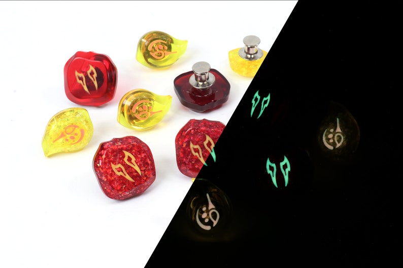 May include: Set of red and yellow dice with glow-in-the-dark features. The dice have a variety of symbols, including flames and a crescent moon. The dice are shown in both normal light and in the dark, highlighting their glow-in-the-dark properties.