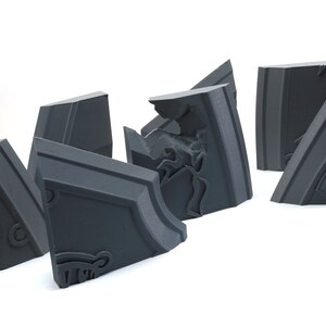 May include: A set of six gray, geometric, 3D printed puzzle pieces. The pieces are designed to fit together to form a larger shape.