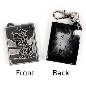 May include: A silver-colored keychain with a black and white image of a creature on the front and a black and white abstract design on the back.