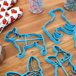 Puede incluir: Un juego de seis cortadores de galletas de pl&aacute;stico azul con forma de perros. Los cortadores est&aacute;n sobre una superficie de madera.