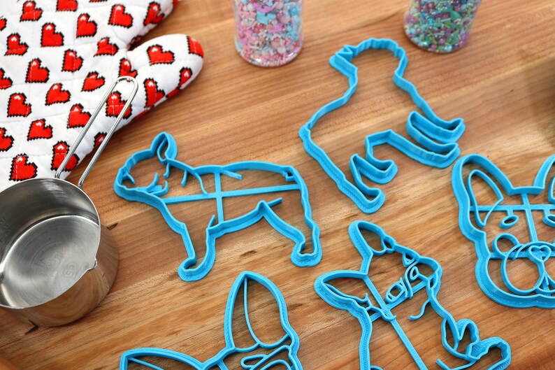 Puede incluir: Un juego de seis cortadores de galletas de pl&aacute;stico azul con forma de perros. Los cortadores est&aacute;n sobre una superficie de madera.