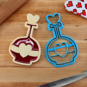 May include: Two cookie cutters in the shape of a bottle with a heart on the front. One cutter is blue and the other is red with white icing.