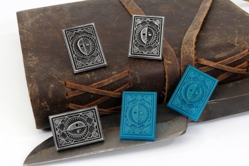 Op de afbeelding: Vier emaillepins met een gestileerd zon- en maandesign. Twee pins zijn zilver en twee zijn blauw.