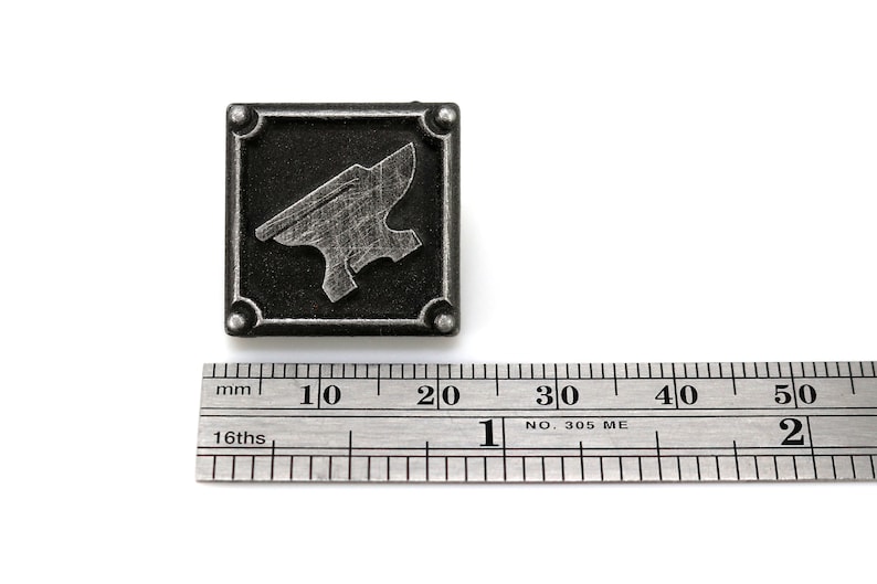 May include: A silver metal pin with a black background and a silver anvil design. The pin is 2 cm wide.