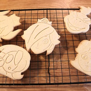 May include: Five unbaked sugar cookies on a wire rack. The cookies are shaped like cartoon faces and have been decorated with a simple outline.