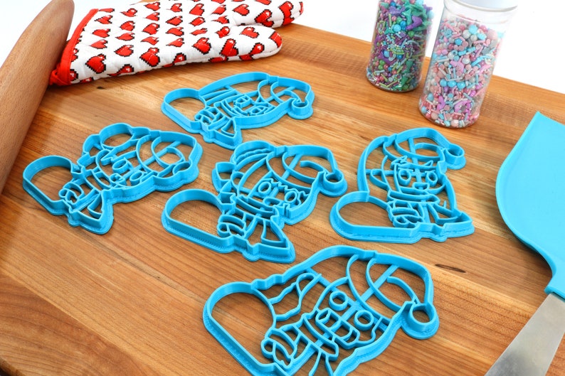 May include: Five blue plastic Christmas cookie cutters shaped like Santa Claus. The cutters are on a wooden surface.