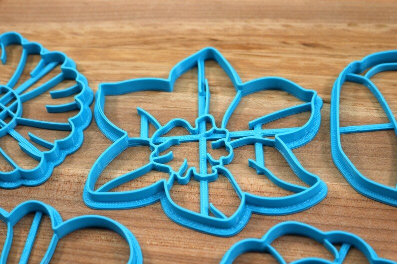 May include: A set of blue plastic cookie cutters shaped like flowers. The cutters are on a wooden surface.