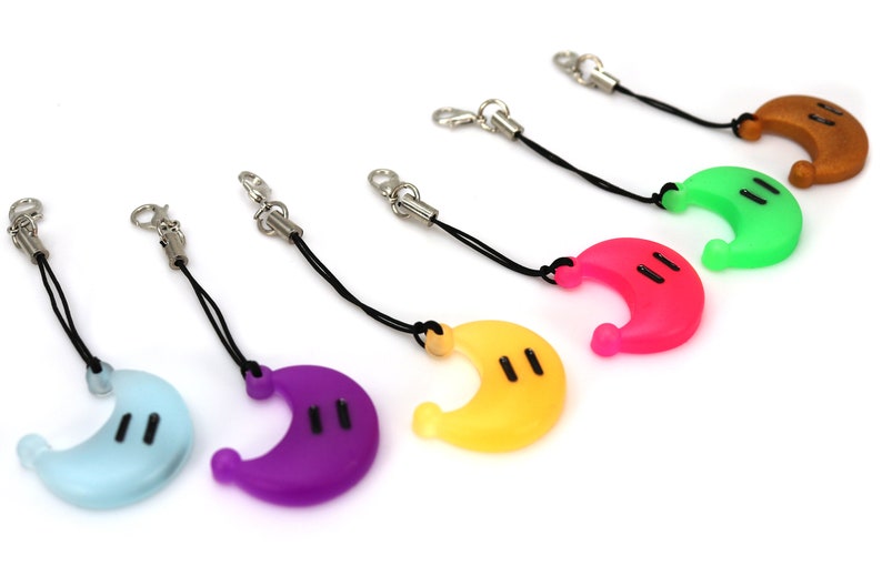 May include: A set of seven colorful crescent moon-shaped phone charms with black eyes. Each charm is attached to a black string with a silver clip.