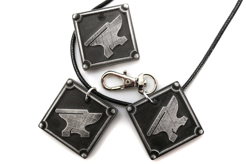 May include: Three silver-colored metal pendants with an anvil design. The pendants are attached to black cords and one has a silver-colored clasp.