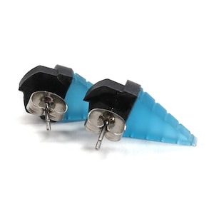 May include: A pair of stud earrings featuring a geometric design. The earrings have a black top section and a light blue, stepped lower section. The earring posts are silver-colored.
