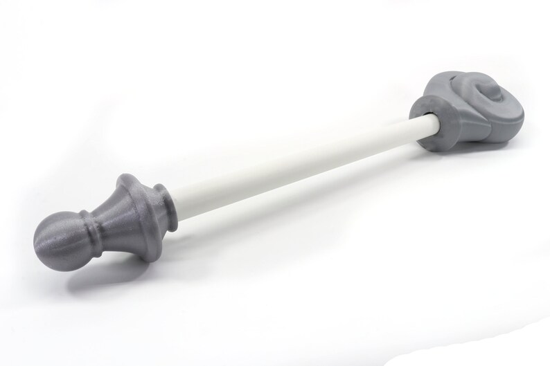 K&ouml;nnte beinhalten: Eine dekorative Gardinenstange mit grauen Endst&uuml;cken und einer wei&szlig;en Stange. Die Endst&uuml;cke haben ein detailliertes, verziertes Design. Die Stange ist etwa 76 cm lang.