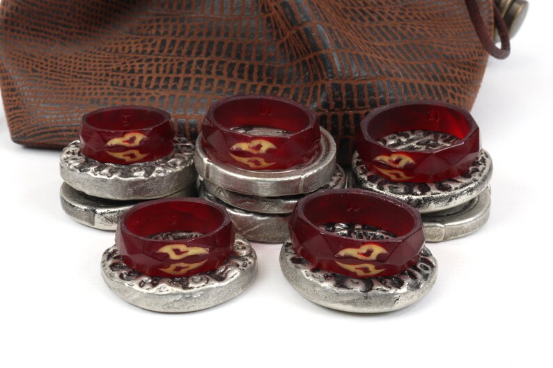 May include: A set of eight red and silver game pieces with a stylized flame design. The pieces are stacked and arranged on a white surface.