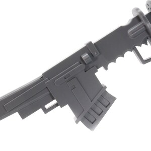 Puede incluir: Una pistola de juguete de pl&aacute;stico gris con una culata plegable y un cargador. La pistola tiene un dise&ntilde;o futurista con una empu&ntilde;adura dentada y una superficie texturizada.