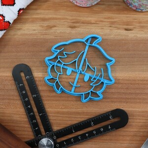 May include: Blue plastic cookie cutter shaped like a cartoon character with short hair and a smiling face.
