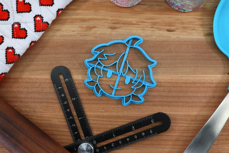 May include: Blue plastic cookie cutter shaped like a cartoon character with short hair and a smiling face.