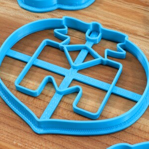 Puede incluir: Un cortador de galletas de pl&aacute;stico azul con forma de casa con techo y chimenea. El cortador tiene una superficie texturizada y est&aacute; dise&ntilde;ado para hacer galletas.