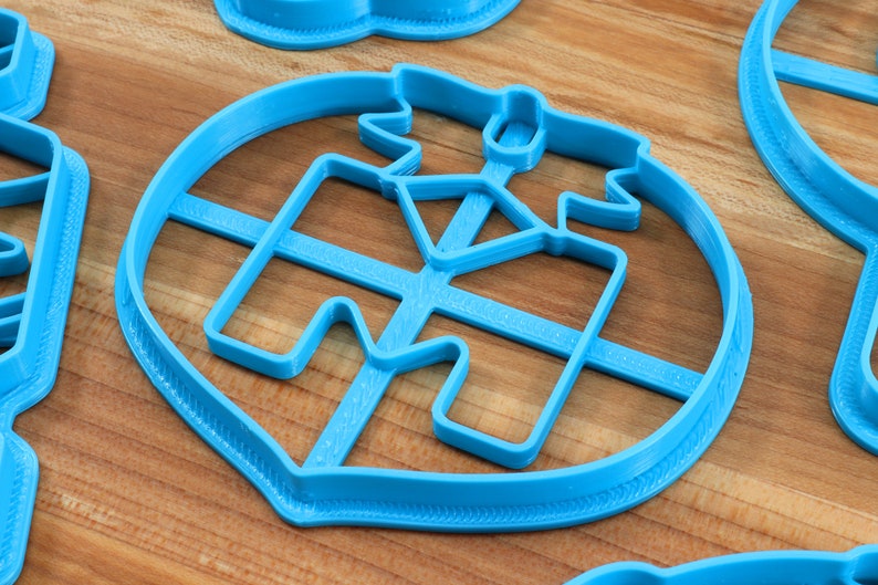 Puede incluir: Un cortador de galletas de pl&aacute;stico azul con forma de casa con techo y chimenea. El cortador tiene una superficie texturizada y est&aacute; dise&ntilde;ado para hacer galletas.