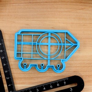 May include: A blue plastic cookie cutter shaped like a pencil with a circle in the middle and wheels on the bottom.