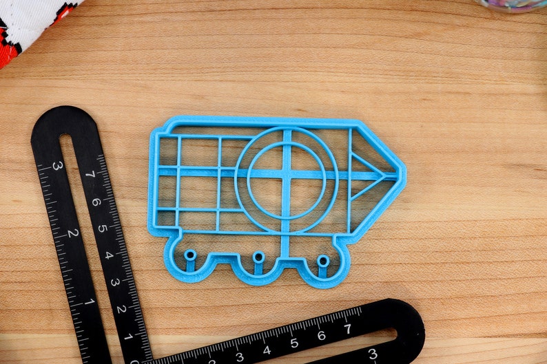 May include: A blue plastic cookie cutter shaped like a pencil with a circle in the middle and wheels on the bottom.