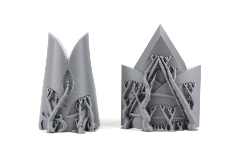 May include: Two gray 3D printed crown-shaped objects with intricate designs. The crowns are made of a textured material and have a detailed pattern of branches and leaves.