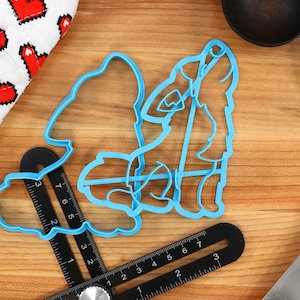 Könnte beinhalten: Zwei blaue Plastik-Ausstecher in Form eines heulenden Wolfes. Die Ausstecher liegen auf einer Holzoberfläche mit einem Lineal und einem blauen Spatel.