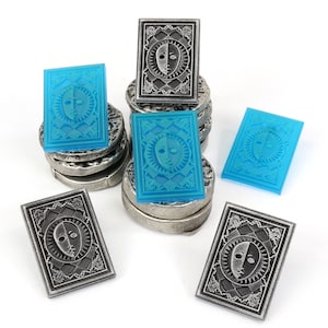 Op de afbeelding: Een stapel zilveren en blauwe tokens met een ontwerp van een gezicht met een lichte en een donkere kant. De tokens zijn in een stapel gerangschikt met enkele aan de zijkant.