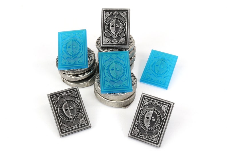 Op de afbeelding: Een stapel zilveren en blauwe tokens met een ontwerp van een gezicht met een lichte en een donkere kant. De tokens zijn in een stapel gerangschikt met enkele aan de zijkant.