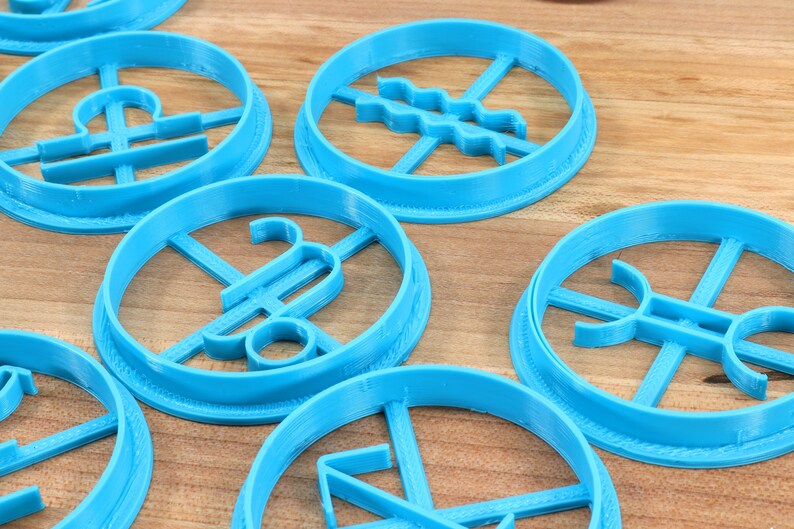 May include: A set of blue plastic cookie cutters shaped like astrological signs. The signs include Libra, Aquarius, Pisces, Sagittarius, and Capricorn.