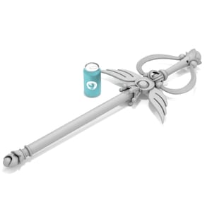 May include: A white, ornate wand with a heart-shaped handle and a winged design. The wand is lying on a white surface next to a blue can.