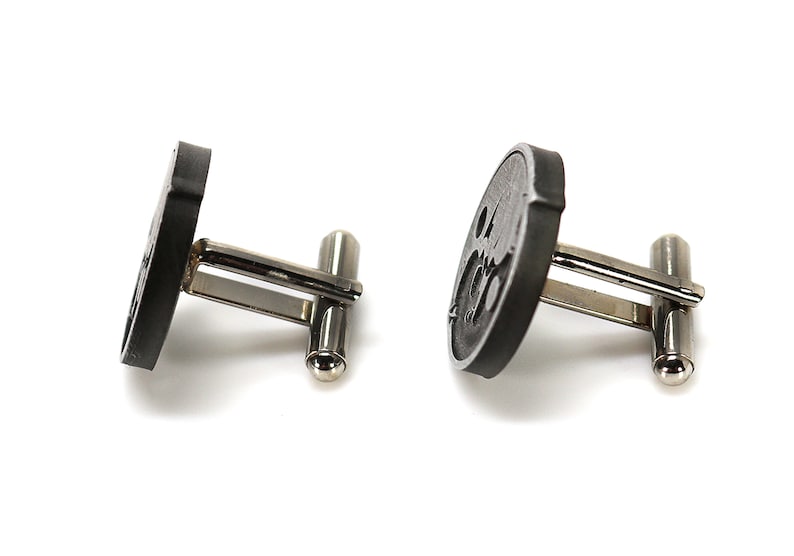 May include: A pair of black cufflinks with a circular design. The cufflinks have a silver metal backing.