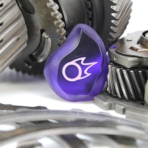 May include: A close-up of a purple glass gear shift knob with a white flame design. The knob is surrounded by metal gears.