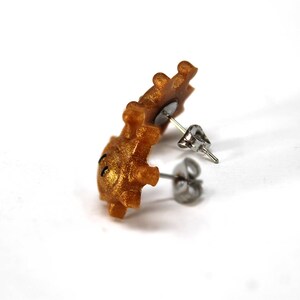 May include: Gold-coloured stud earrings with a small, detailed design. The earrings are made of polymer clay and have a post and butterfly backing.