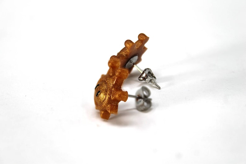 May include: Gold-coloured stud earrings with a small, detailed design. The earrings are made of polymer clay and have a post and butterfly backing.
