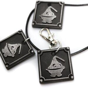 May include: Three silver-colored pendants with a black background and a cartoon character design. The pendants are attached to a black cord necklace with a silver clasp.