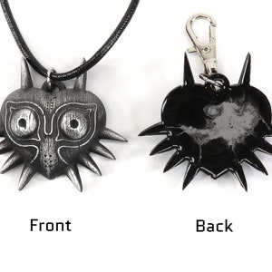 May include: A silver-colored Majora's Mask pendant necklace with a black cord. The back of the pendant is black. The pendant is also available as a keychain.