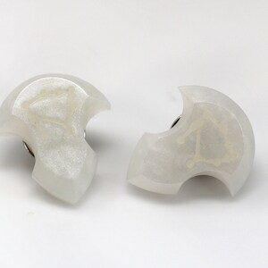 May include: Two white resin earrings with a crescent moon shape and a silver metal post. Each earring has a white design inside the crescent moon.