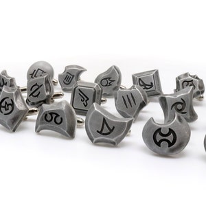 May include: A set of 16 silver cufflinks featuring various symbols, each with a unique design. The cufflinks are arranged in a scattered pattern on a white background.