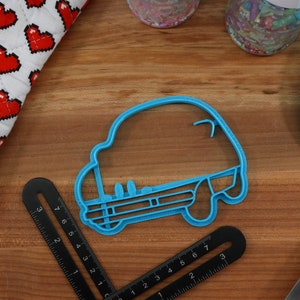 May include: A blue plastic cookie cutter shaped like a car. The cutter is on a wooden surface.
