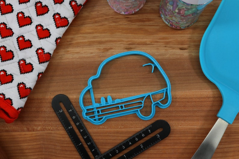 May include: A blue plastic cookie cutter shaped like a car. The cutter is on a wooden surface.