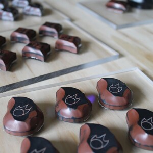 May include: Close-up of several small, brown, ceramic pieces with a black flame design. The pieces are arranged on a wooden surface.