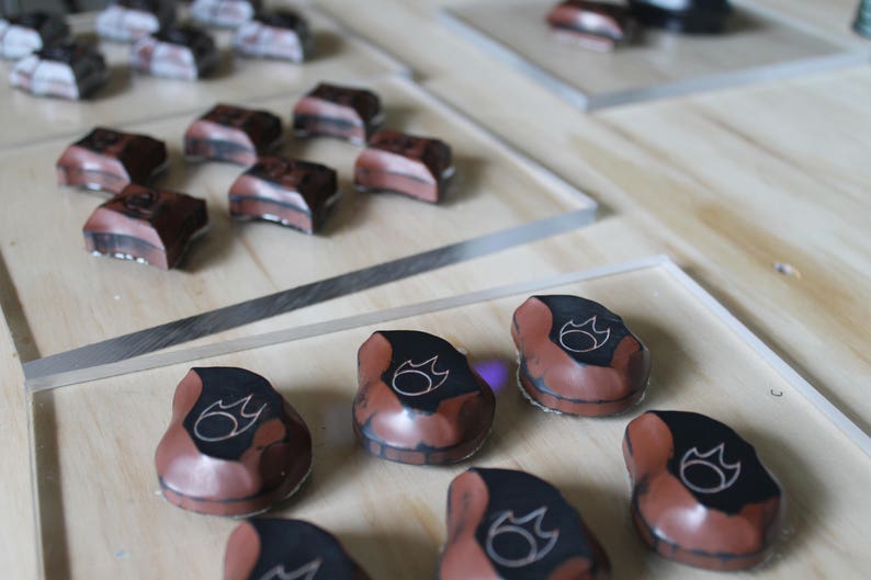 May include: Close-up of several small, brown, ceramic pieces with a black flame design. The pieces are arranged on a wooden surface.
