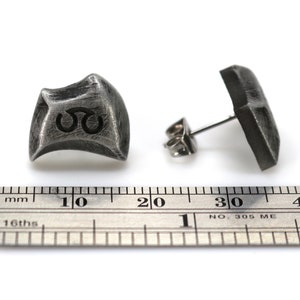 May include: A pair of silver earrings with a textured, geometric design. The earrings are approximately 1 cm in diameter and have a post back.
