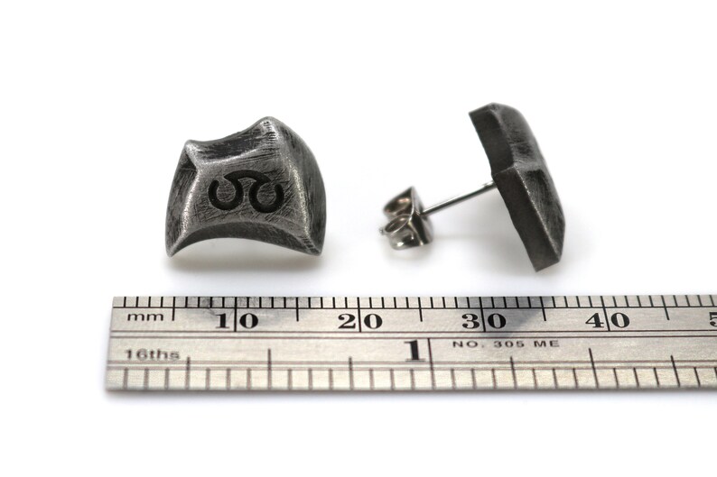 May include: A pair of silver earrings with a textured, geometric design. The earrings are approximately 1 cm in diameter and have a post back.