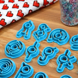 May include: A set of 15 blue plastic cookie cutters shaped like different geometric designs. The cutters are arranged on a wooden surface.