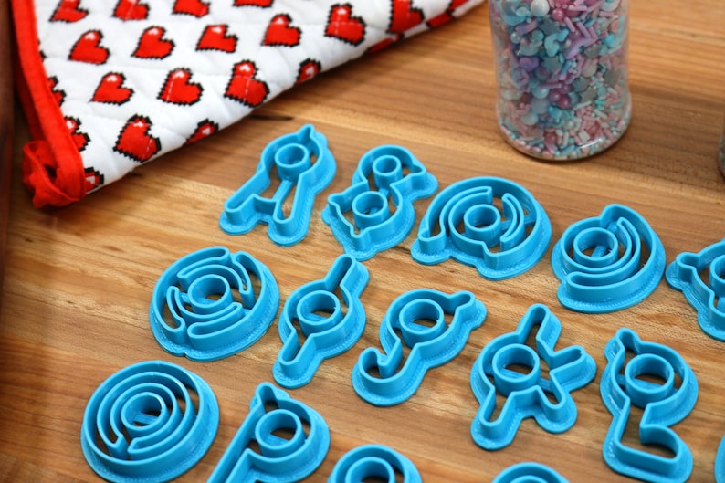 May include: A set of 15 blue plastic cookie cutters shaped like different geometric designs. The cutters are arranged on a wooden surface.