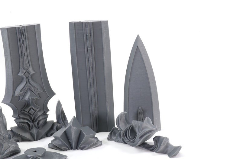 May include: A set of five gray 3D printed pieces that make up a sword. The pieces include the blade, hilt, pommel, and two decorative pieces.