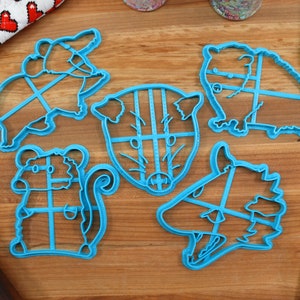 May include: A set of six blue plastic cookie cutters shaped like different animals. The cutters are on a wooden surface.